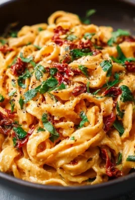 Creamy vegan sun-dried tomato pasta dish garnished with fresh herbs.