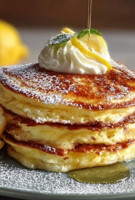 Fluffy lemon ricotta pancakes stacked on a plate with syrup and lemon zest