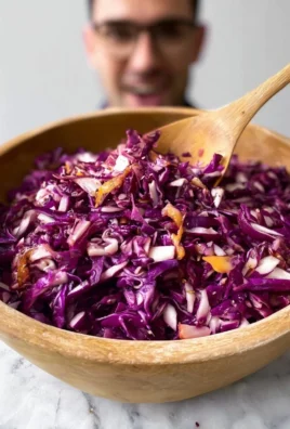 A colorful bowl of red cabbage slaw with carrots and green herbs.