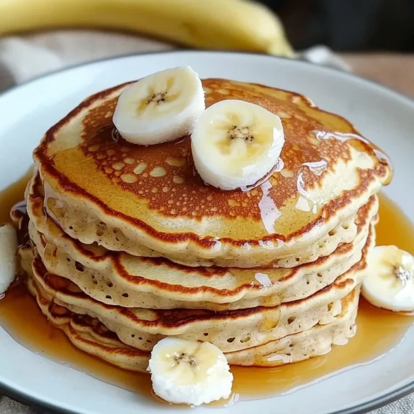 Fluffy 3 ingredient banana pancakes served on a plate with syrup and berries.