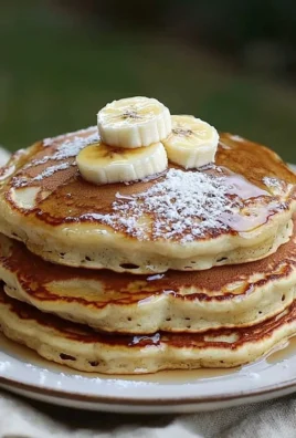 Stack of fluffy banana pancakes drizzled with syrup and topped with sliced bananas