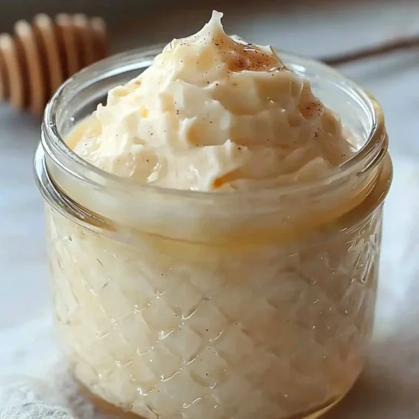 A jar of whipped honey with a wooden dipper, showcasing its creamy texture.