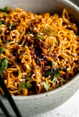 Bowl of spicy ramen noodles garnished with vegetables and herbs