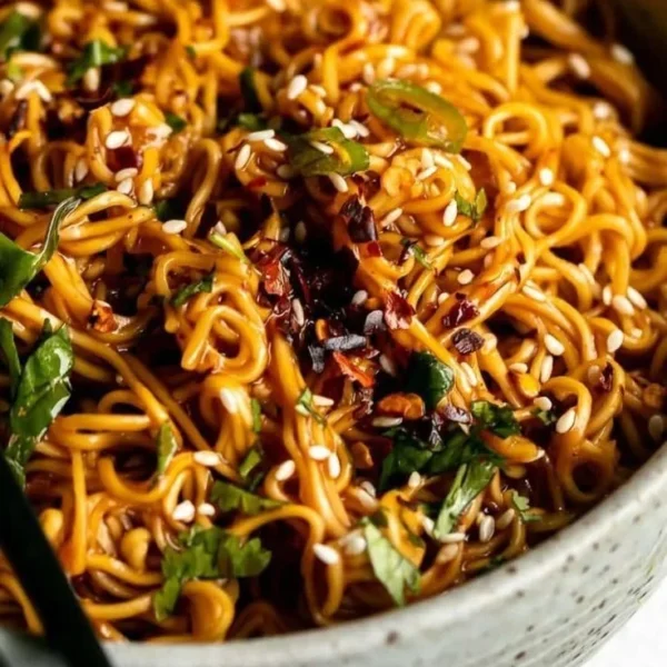Bowl of spicy ramen noodles garnished with vegetables and herbs
