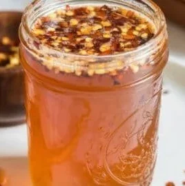 Homemade hot honey in a jar with chili peppers and a drizzle on a plate.