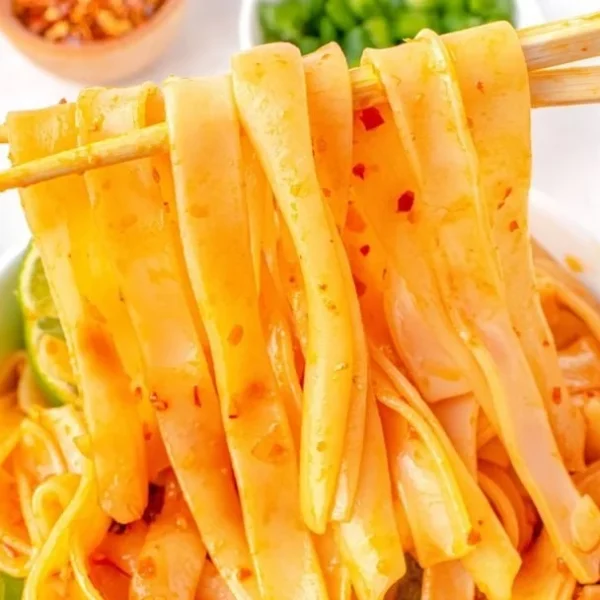 A bowl of hot and spicy noodles garnished with herbs and chilies