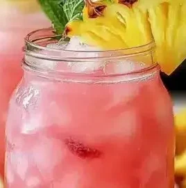 A glass of Pineapple Pink Lemonade with tropical fruits and fresh mint