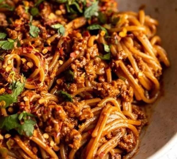 Bowl of spicy Korean Gochujang noodles with fresh veggies and garnish.