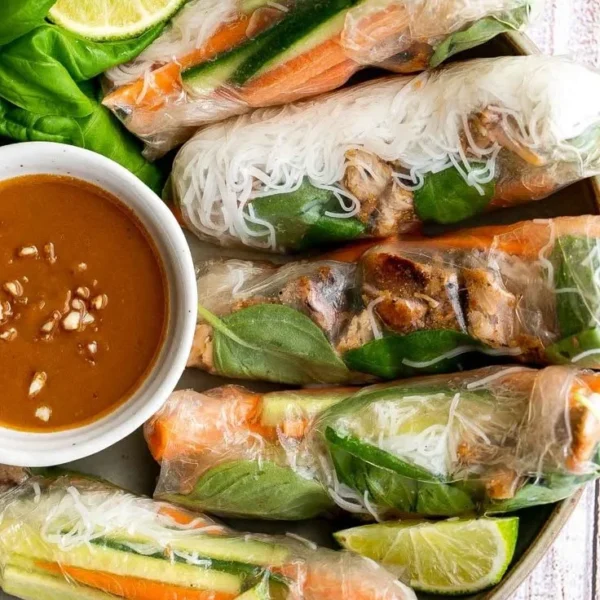 Vietnamese summer rolls with chicken served on a plate with fresh herbs and dipping sauce.