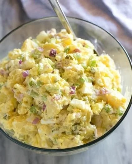 Creamy potato salad served in a bowl with fresh herbs and seasoning.