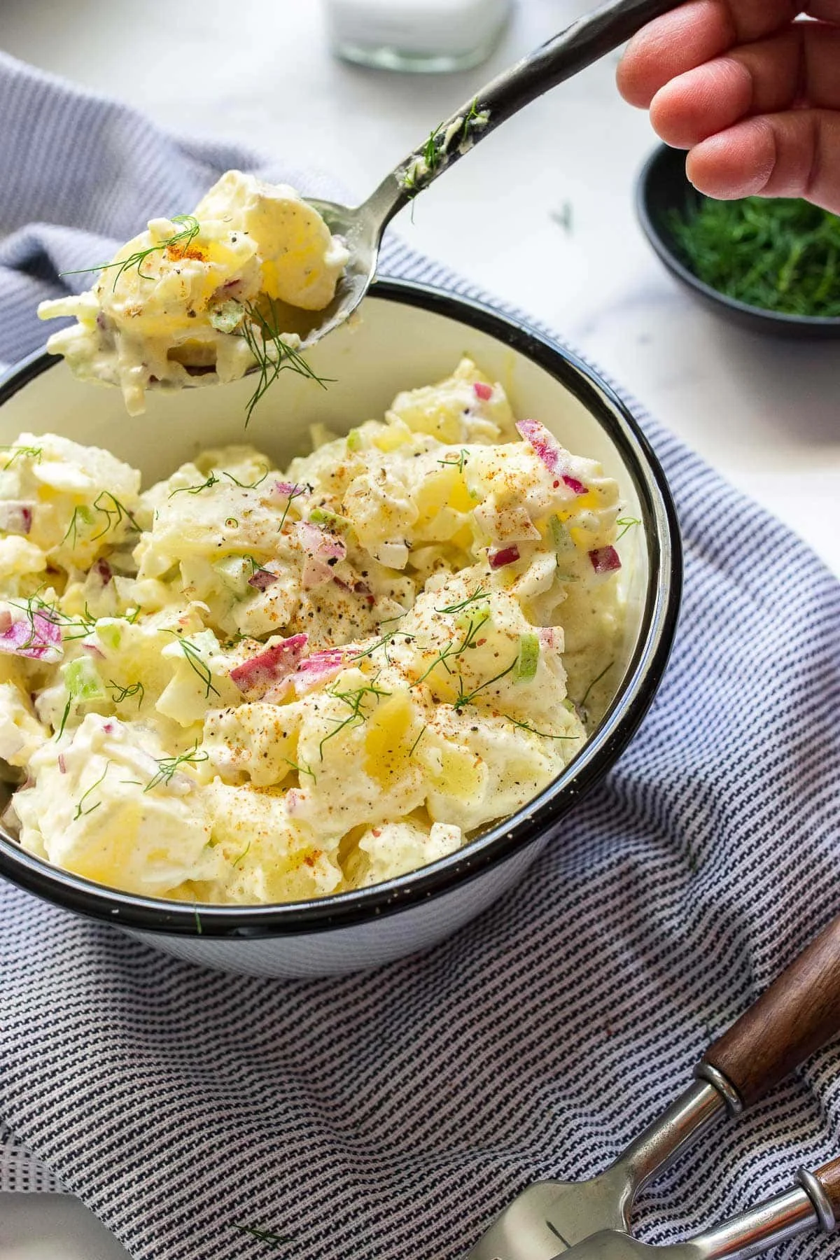 A bowl of creamy potato salad garnished with herbs and spices.